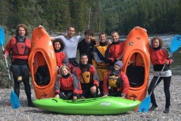Group of beginner whitewater kayak students taking group photo with gear on river's edge