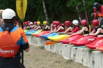 long row of intermediate kayakers sitting on the beach listening to instructors